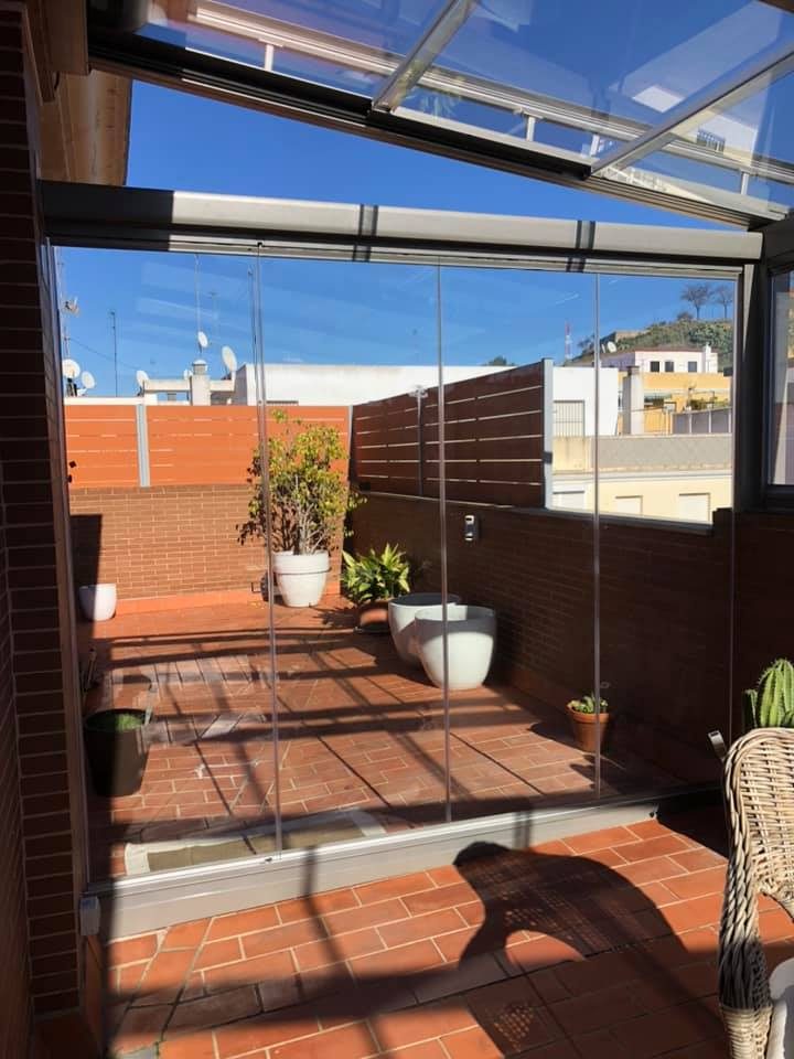 Cerramiento de cristal corredero en terraza con macetas y vistas a la ciudad